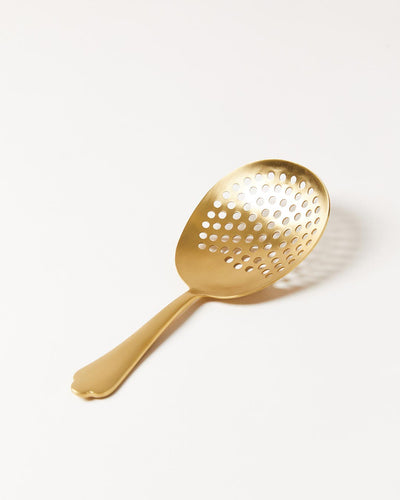 Brushed-gold perforated cocktail strainer with a broad oval bowl and short decorative handle.