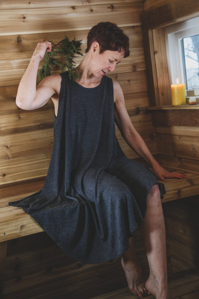 Woman wearing a charcoal merino wool sauna dress while seated in a Finnish sauna, designed for heat, cold plunge, and recovery.