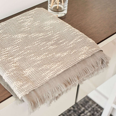 Close product view of the folded Flo Gray throw showing its woven white pattern and hand-finished fringe