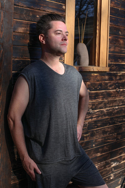 Man wearing a sleeveless merino wool sauna tee outside a sauna, designed for heat, recovery, and wellness rituals.