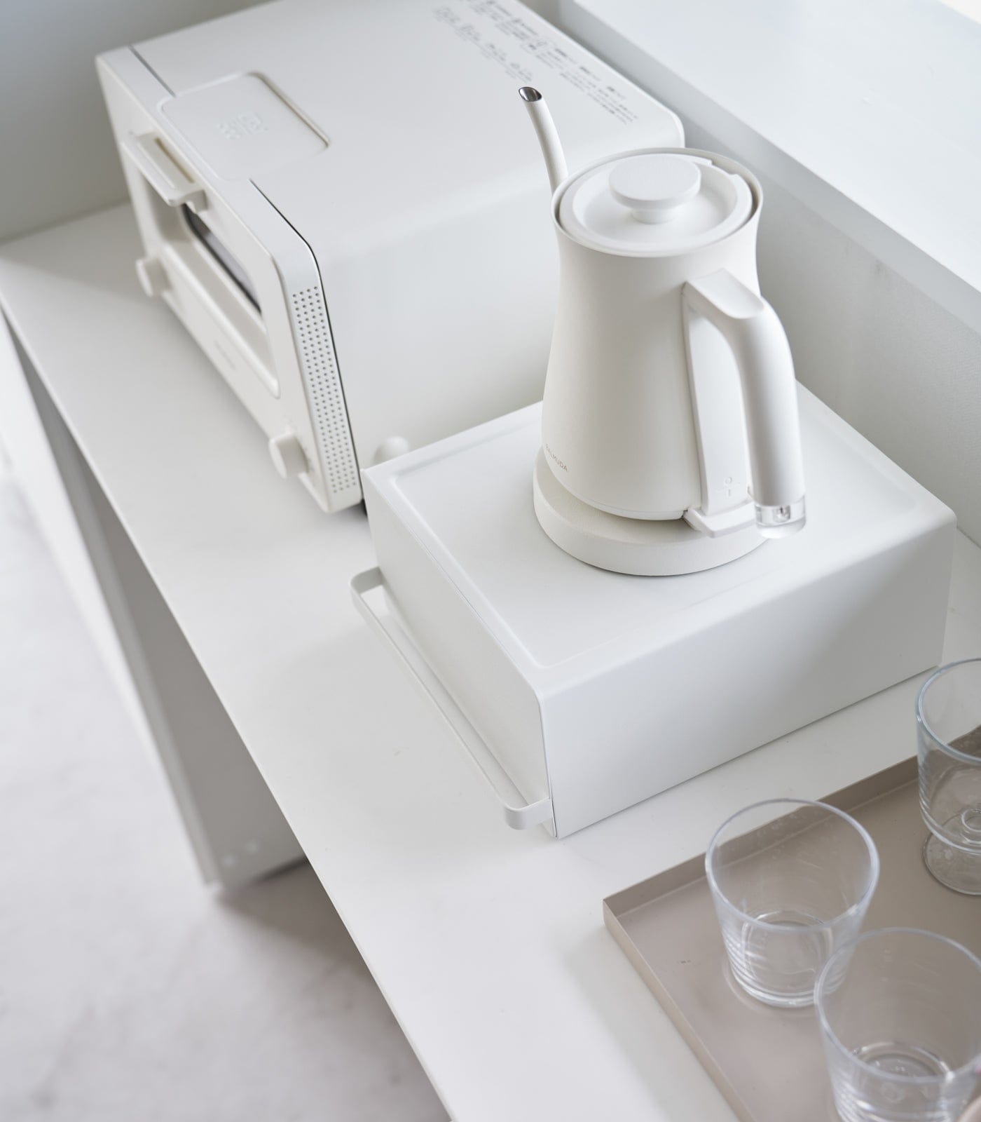 White electric kettle on a white surface with a white appliance in the background