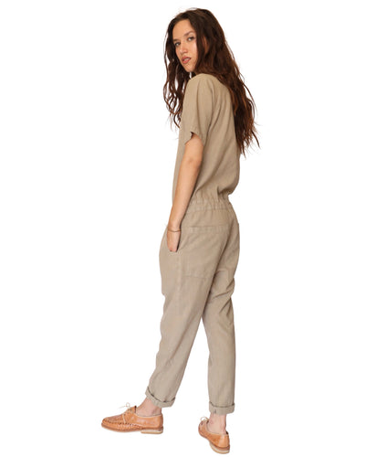 Three-quarter rear view of a model wearing the tan short-sleeve jumpsuit.