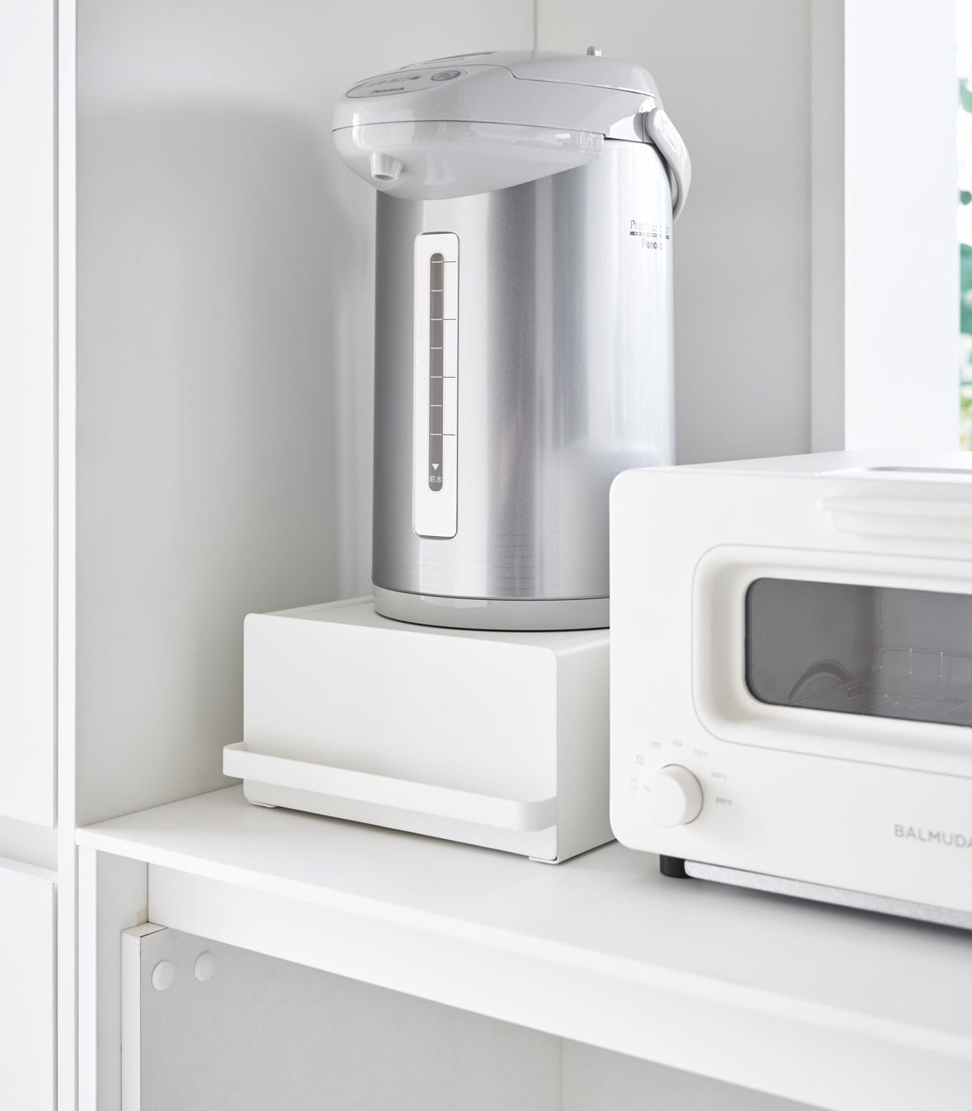 Silver electric kettle on a white shelf next to a white microwave.
