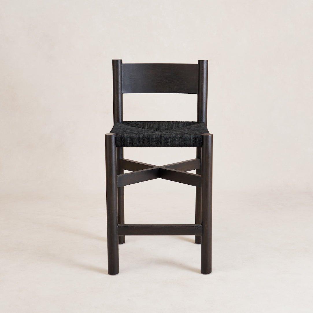 A black Nonna counter stool with a spacious seat constructed from woven jute and a gently curved lower backrest, standing on a white background.