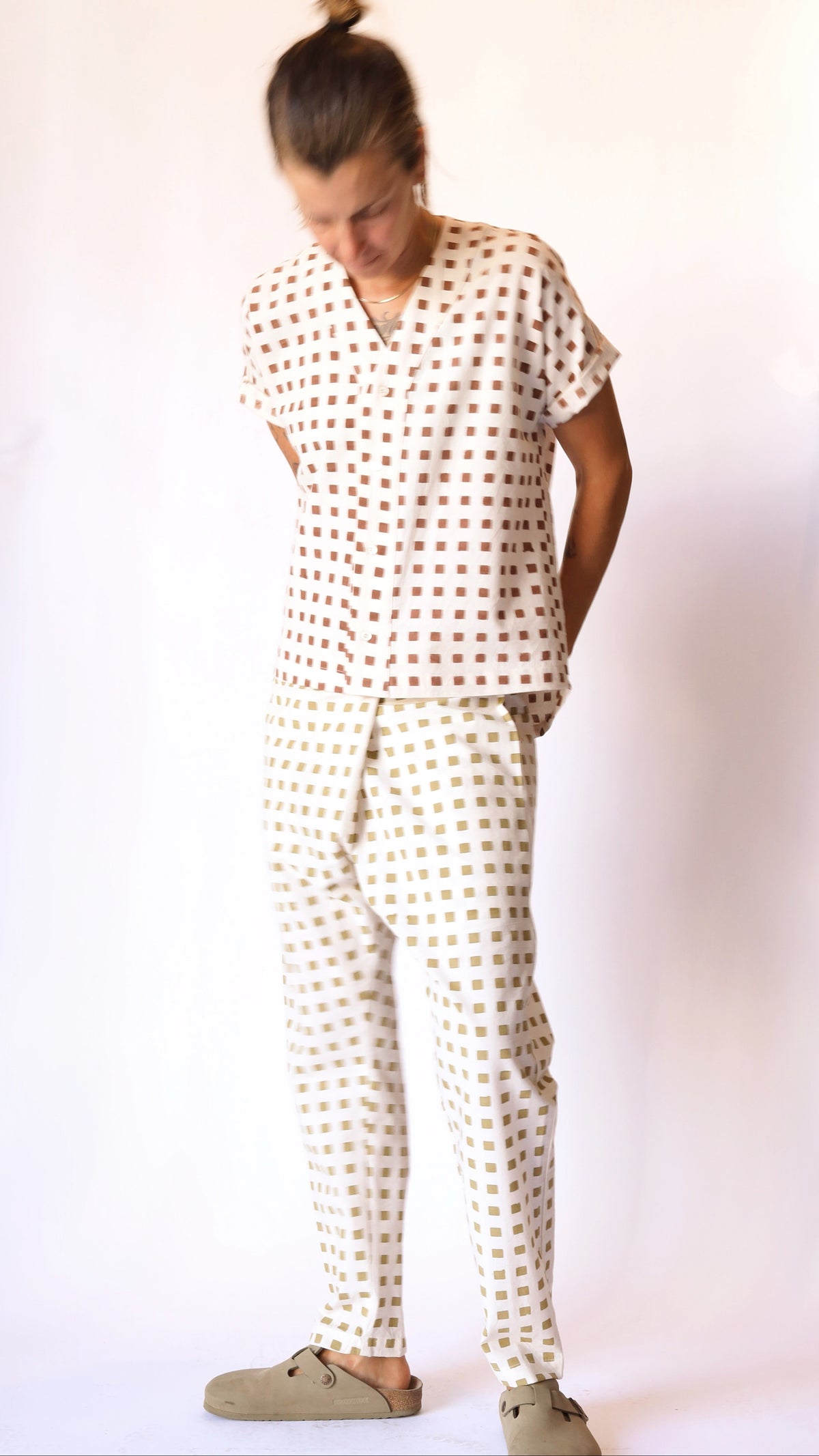 Model wearing a cream short-sleeve baseball shirt with rust-red hand-block-printed squares and matching cream patterned pants.