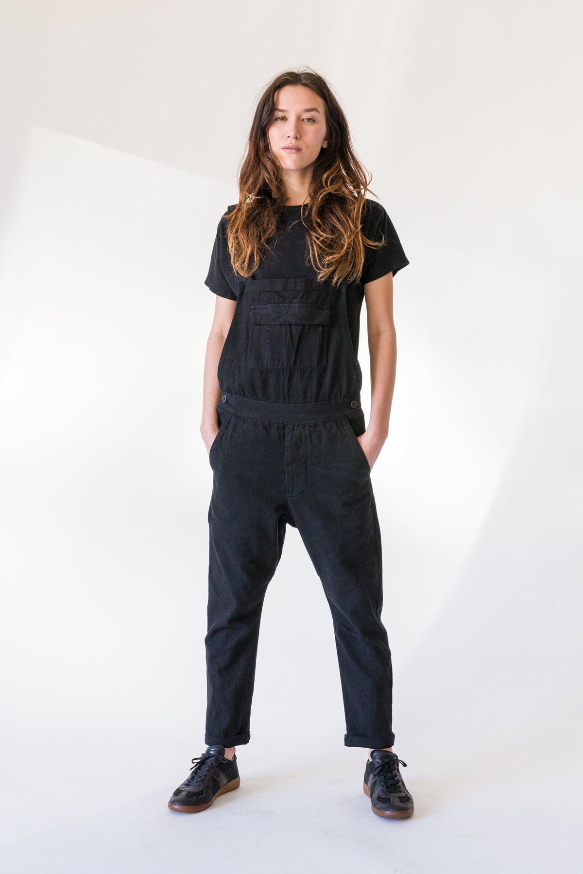 Model wearing black overalls over a black T-shirt with black shoes.