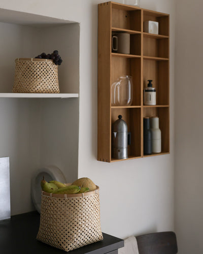 Bamboo baskets used for storage and produce beside a wall-mounted wooden kitchen organizer.