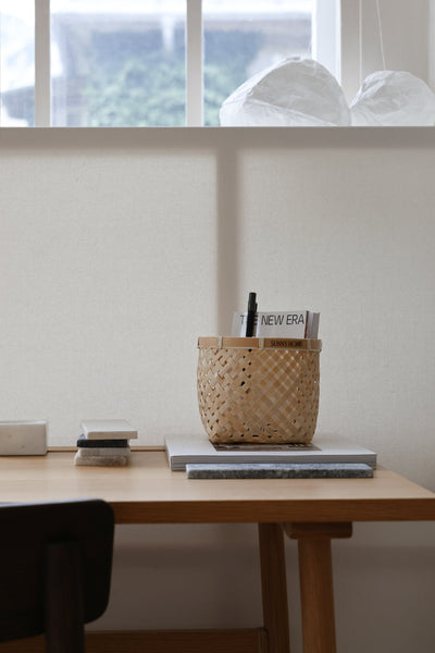 Wider view of a Muko basket holding writing tools on a tidy wooden desk beneath a window.