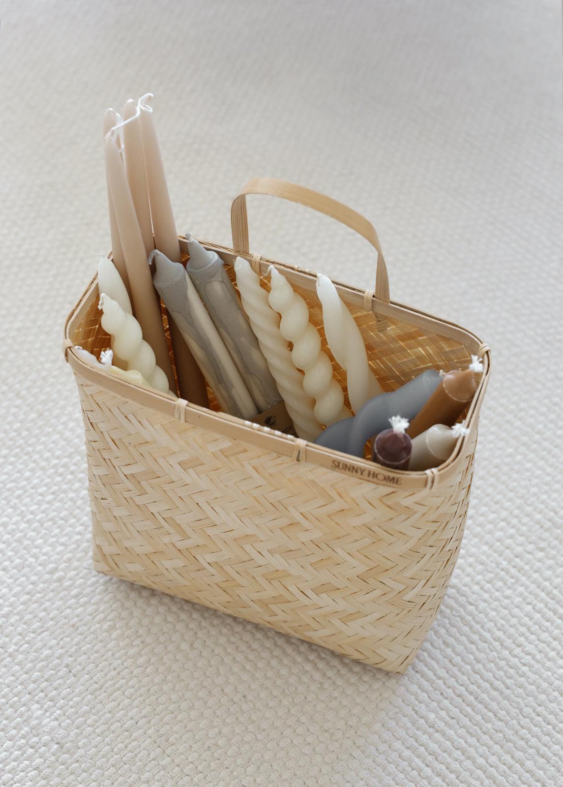 Sapa basket holding decorative taper candles and small accessories on a light surface.