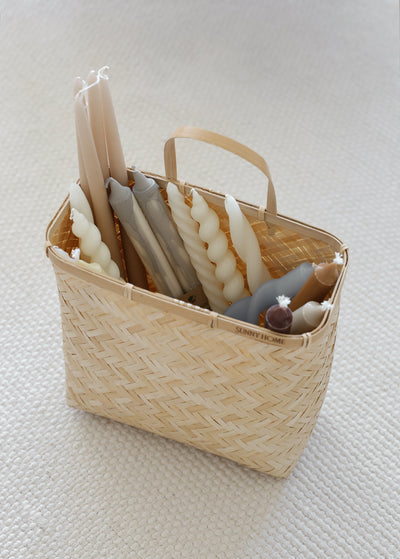 Sapa basket holding decorative taper candles and small accessories on a light surface.