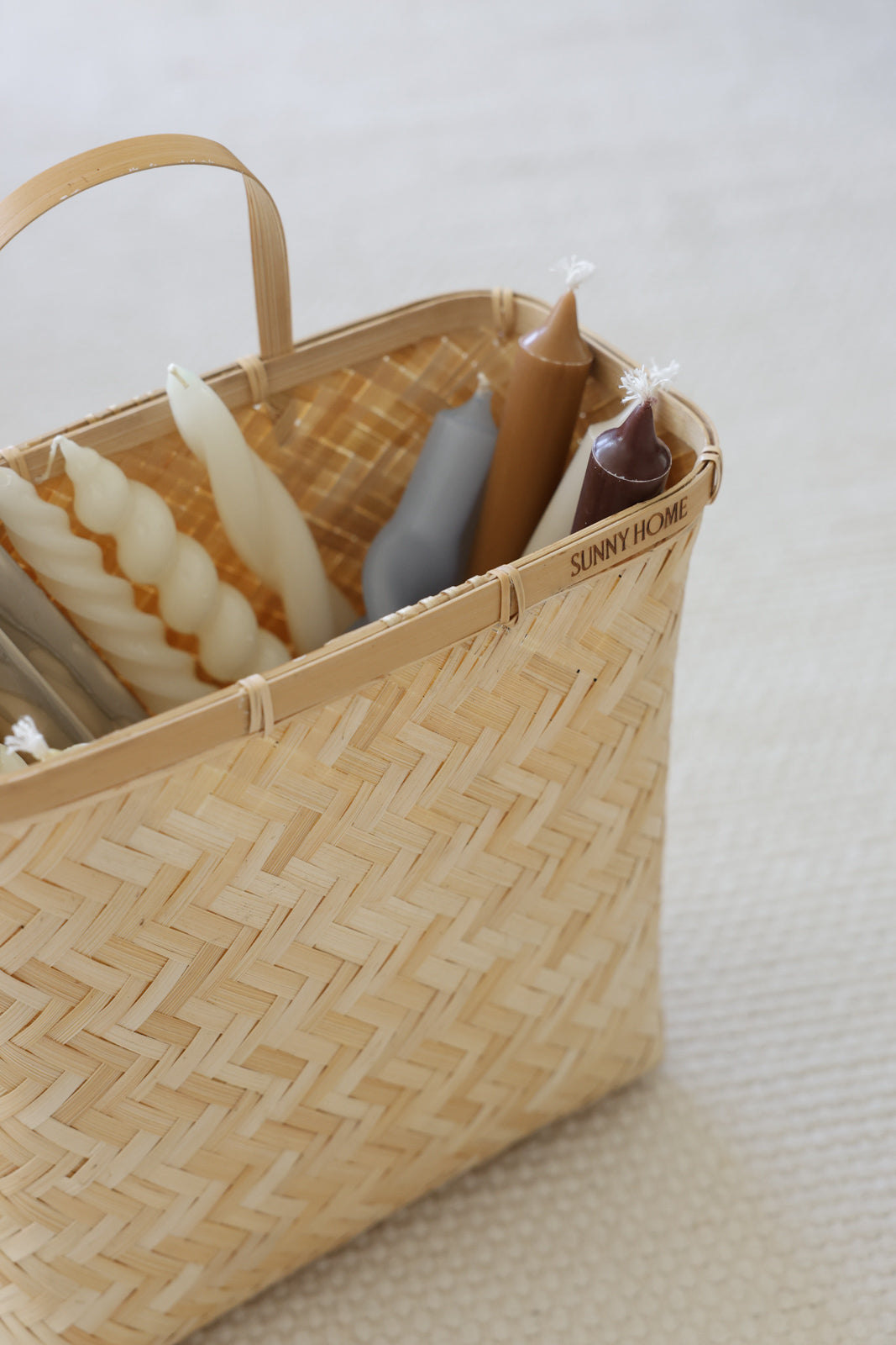 Close view of the woven basket filled with twisted candles and wrapped household items.
