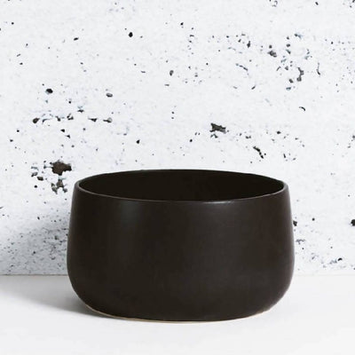 Stoneware serving bowl 120 oz in Matte Black against textured concrete background