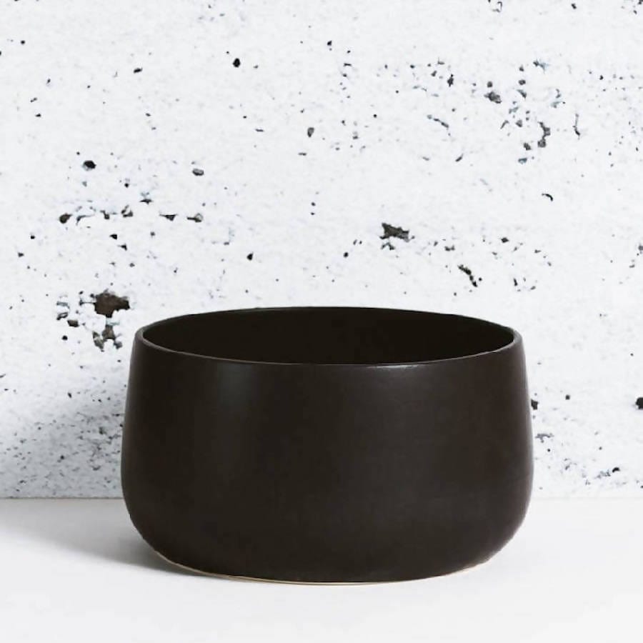 Stoneware serving bowl 120 oz in Matte Black against textured concrete background