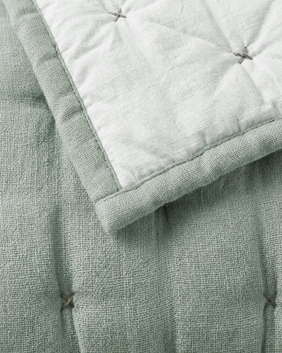 Close-up of the sage quilt’s textured surface and tufted stitches, with the pale reverse folded over a matching green border.