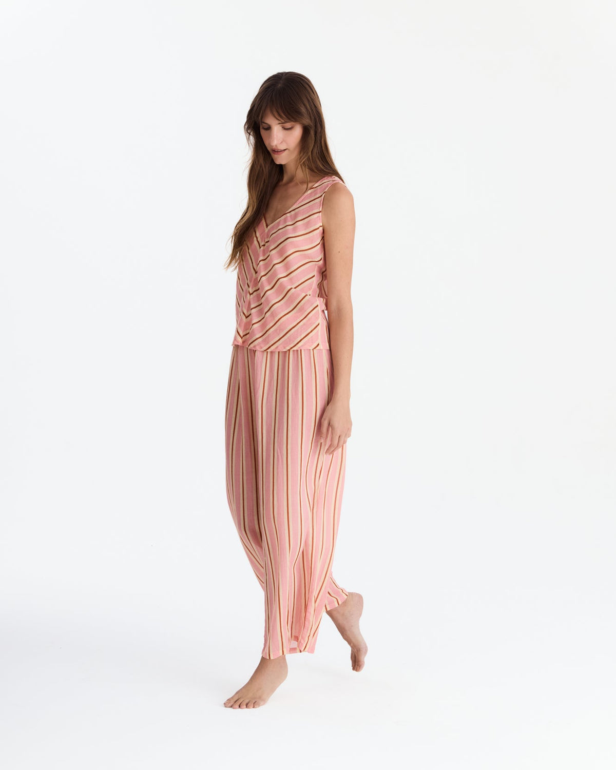 Angled full-length view of the model looking down with one foot lifted, showing the flowing striped pants.