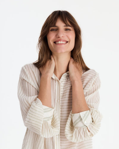 Smiling model holding the shirt’s collar, showing its contrasting stripe panels, buttons, and wide sleeve cuffs.