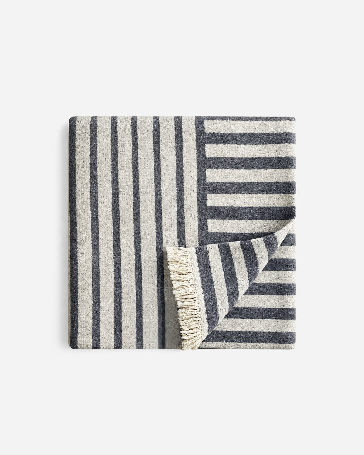 Folded cream and charcoal striped Riva beach blanket, with contrasting stripe directions and a turned-back corner revealing cream fringe.