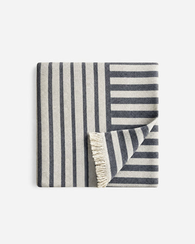 Folded cream and charcoal striped Riva beach blanket, with contrasting stripe directions and a turned-back corner revealing cream fringe.