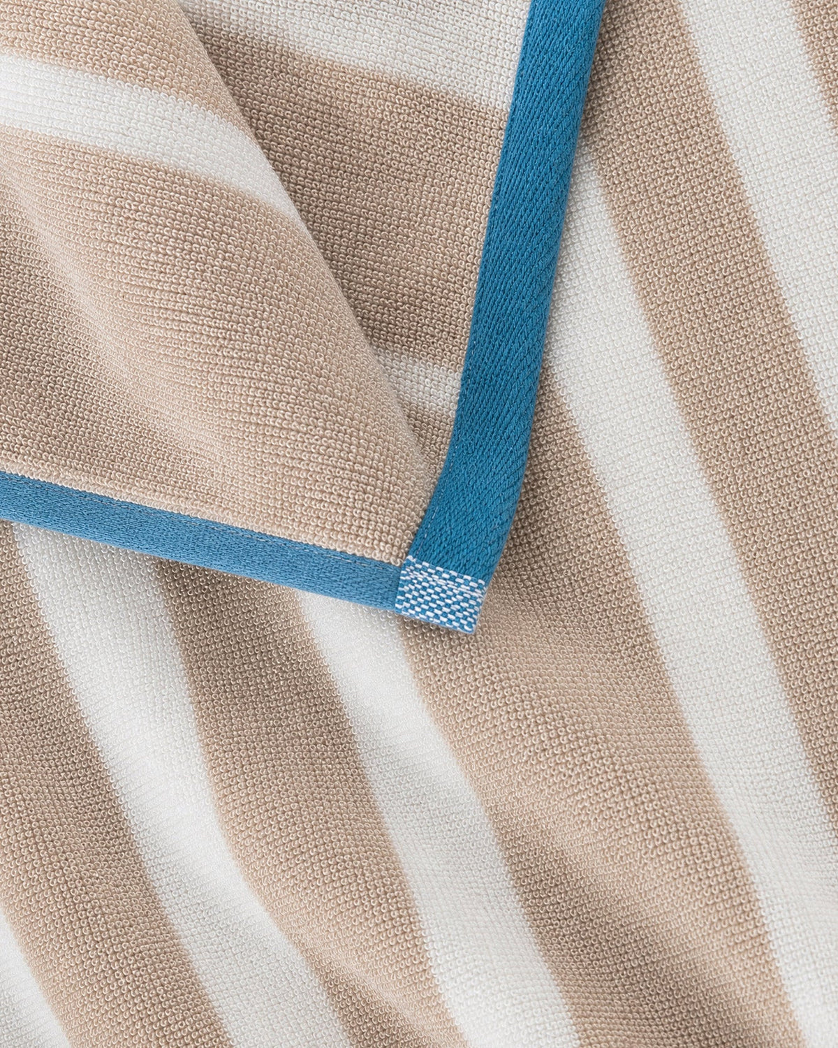 Close-up of the blanket’s woven beige and cream stripes and loosely knotted cream tassels.