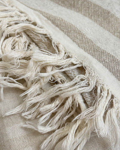 Close-up of the blanket’s woven beige and cream stripes and loosely knotted cream tassels.