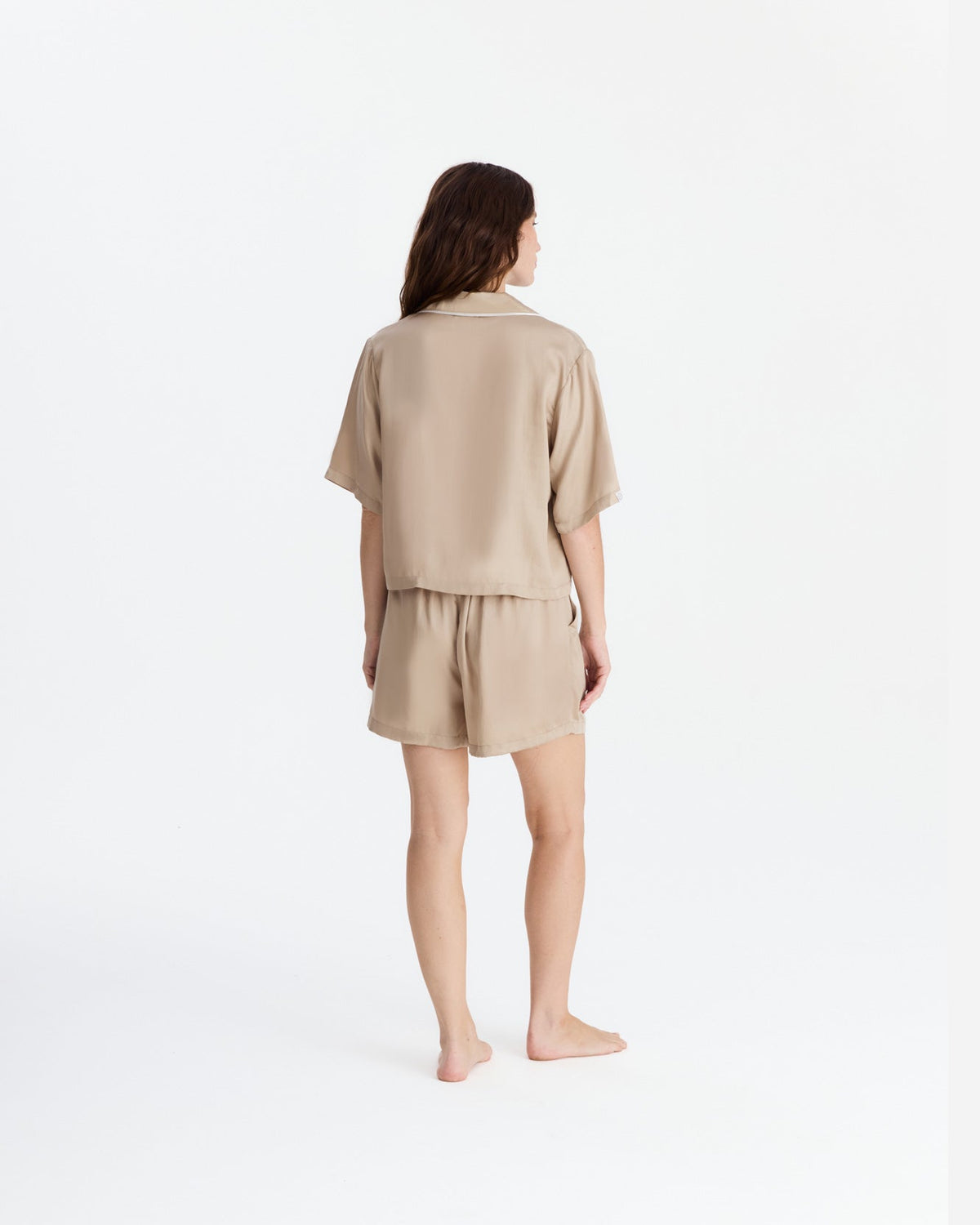 Back view of the beige pajama set, showing the shirt’s straight hem and relaxed fit above matching shorts with a gathered waistband.