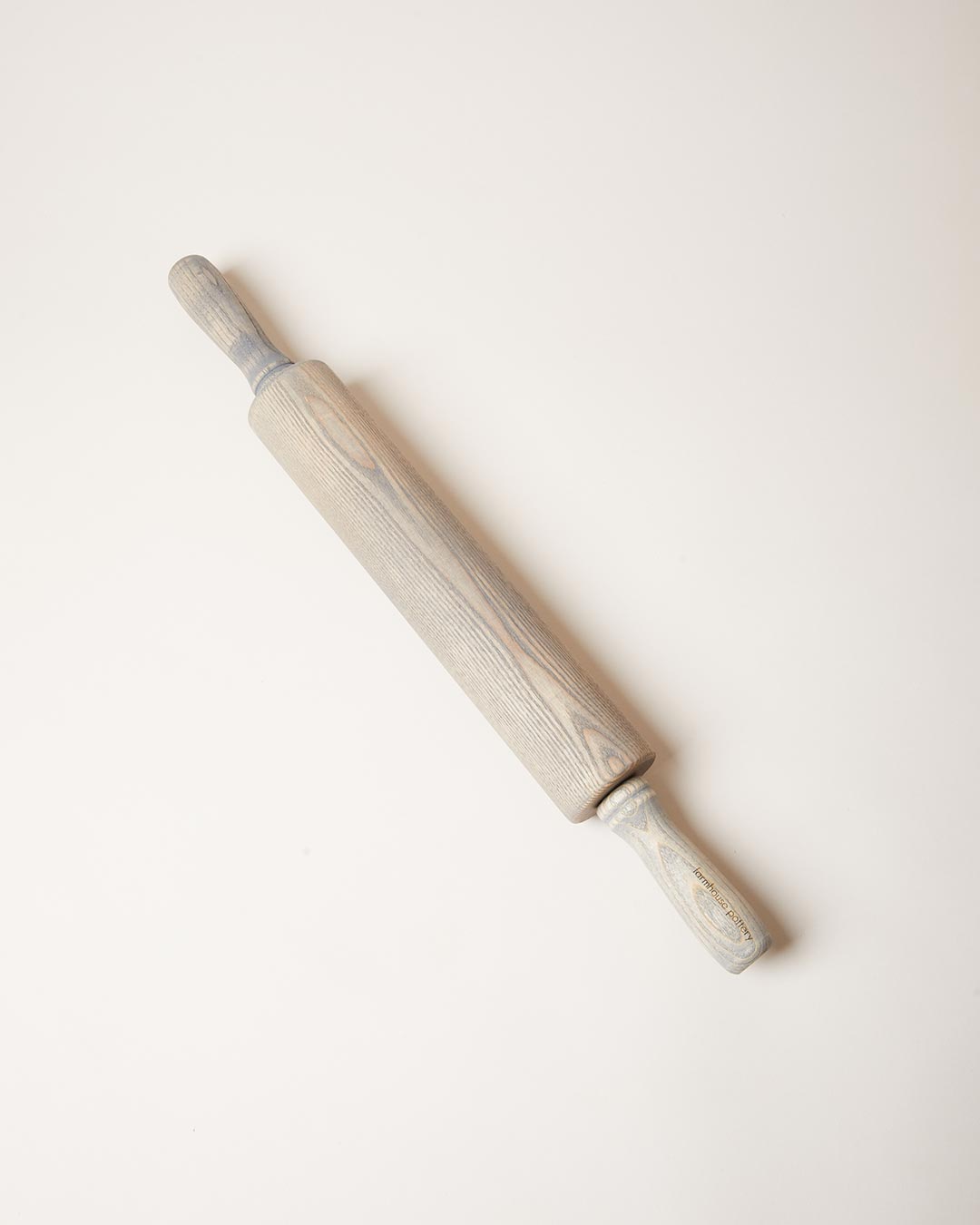 Gray-washed ash rolling pin displayed diagonally, with visible wood grain running through its muted finish.
