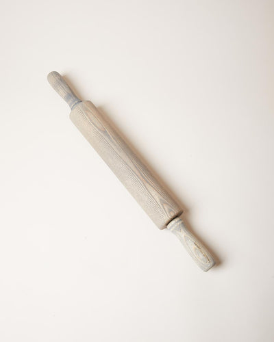 Gray-washed ash rolling pin displayed diagonally, with visible wood grain running through its muted finish.