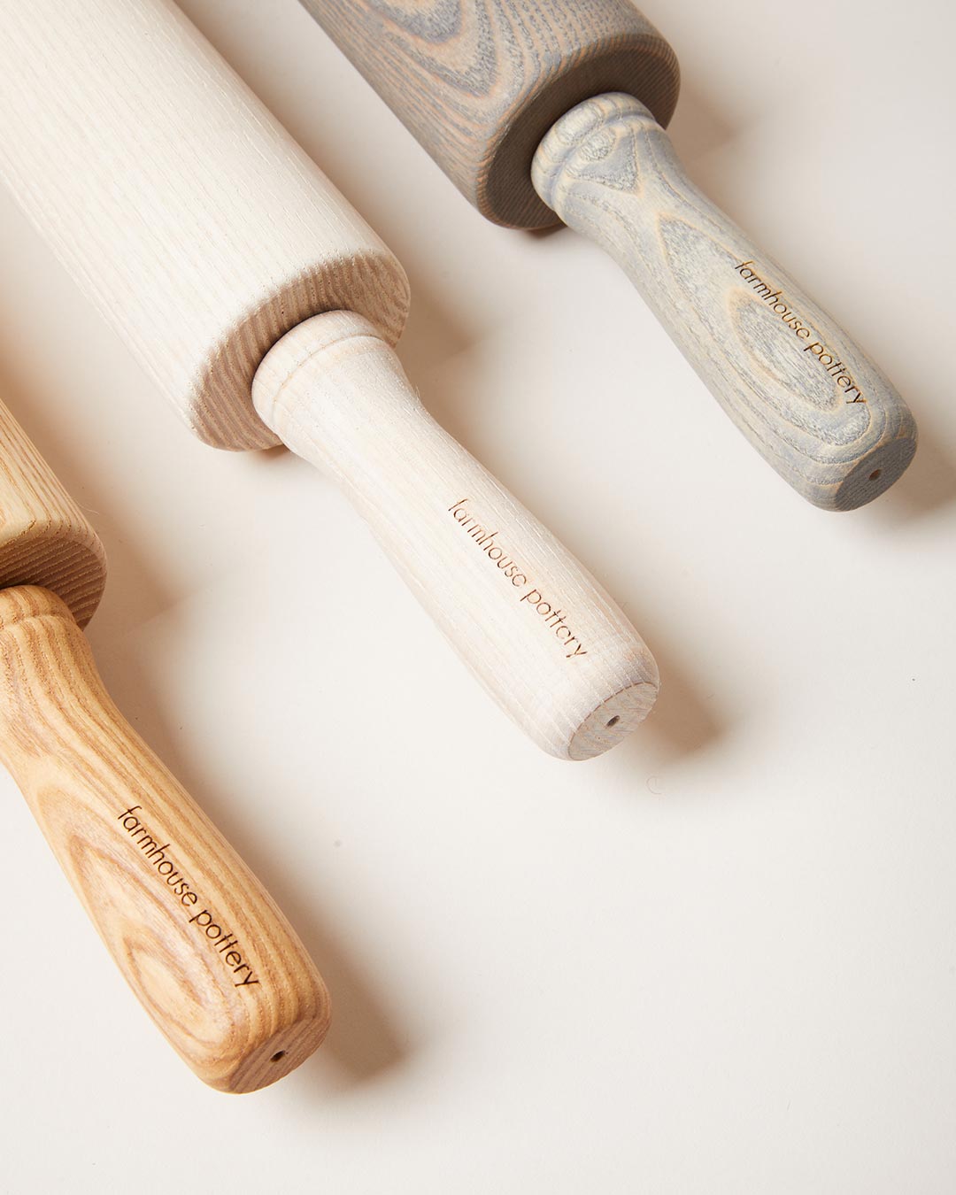 Close-up of natural, whitewashed, and gray-washed ash rolling-pin handles, showing the wood grain and carved grip details.