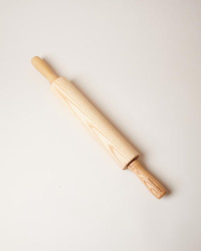 Natural honey-colored ash rolling pin displayed diagonally, showing prominent flowing wood grain along the barrel and handles.