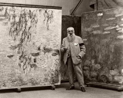 Black-and-white archival photograph of an artist standing beside large abstract canvases.