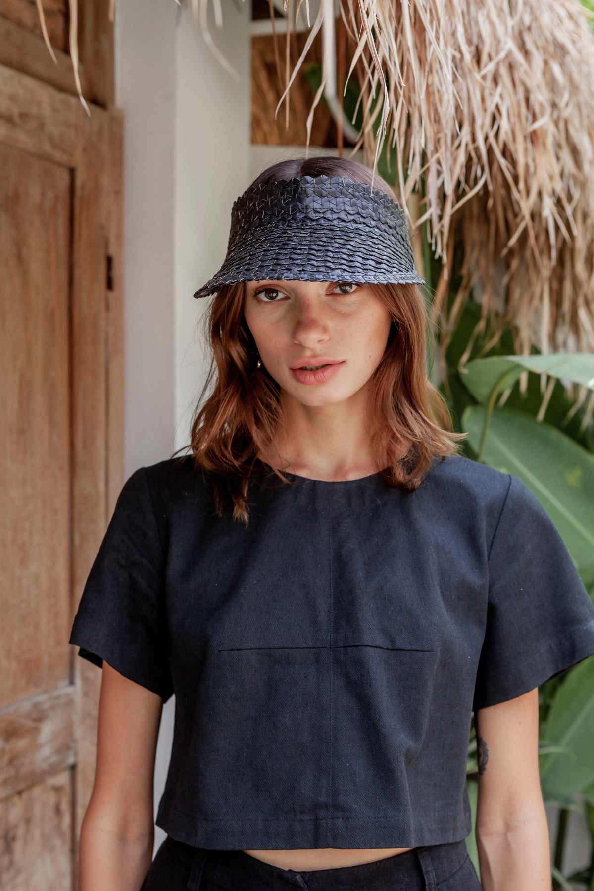Village Thrive Rattan Sun Visor, black palm leaf, worn by a model standing.